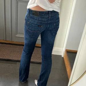 Mörkblå lågmidjade bootcut jeans från Lee - Lågmidjade mörkblå jeans från Lee som jag har sytt till bootcut. Kan inte hitta storlek men skulle säga 34/36, de är försmå för mig som oftast har M i jeans. Tvärs över midjan är det 38 cm och inte så mycket stretch, och innerbenslängden är 77 cm.
