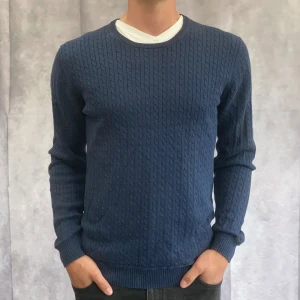 Blå stickad tröja från Tiger of Sweden - Säljer en snygg blå stickad tröja från Tiger of Sweden i lyxig Pima-bomull. Tröjan har ett diskret mönster och är perfekt för både vardag och lite finare tillfällen. Den är långärmad och har en normal passform. Perfekt för höst och vinter!