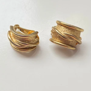 Vintage guldörhängen med textur - Säljer ett par vintage guldfärgade örhängen  med en cool texturerad yta och vridna detaljer. De är clipsörhängen, vilket gör dem perfekta för dig som inte har hål i öronen.Okänd metall.Superfina för att ge en elegant touch till vilken outfit som hels