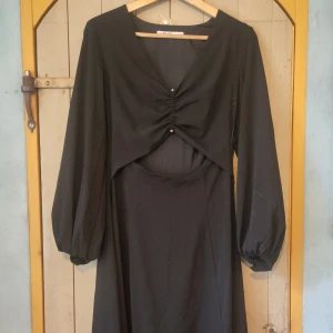 Svart klänning från NA-KD - Säljer en elegant svart klänning från NA-KD i storlek 36. Klänningen har långa ärmar och snygga rynkade detalj framtill som ger en unik look. Perfekt för festliga tillfällen eller en kväll ute. Materialet känns mjukt och bekvämt mot huden. 