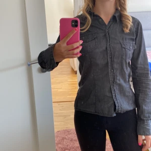 Svart jeansskjorta - Säljer en snygg svart jeansskjorta i storlek S. Skjortan har långa ärmar och knappar framtill. Perfekt för en casual look eller att klä upp med accessoarer. Den är i bra skick och redo för nya äventyr! Armarna kan även knäppas så att de blir kortare (trekvart)