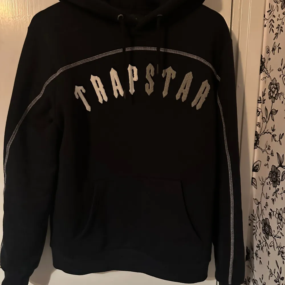 Säljer en svart hoodie från Trapstar med stort tryck på bröstet. Den har en klassisk passform med långa ärmar och en bekväm huva. Perfekt för en avslappnad stil! och byxorna . Tröjor & Koftor.