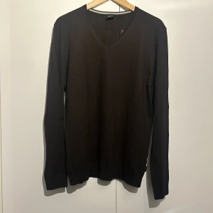 Svart tröja från BOSS - Säljer en stilren svart tröja från BOSS i storlek XL. Tröjan har en klassisk v-ringning och är långärmad, perfekt för både vardag och lite finare tillfällen. Materialet känns mjukt och bekvämt, vilket gör den idealisk för höst och vinter. Passar bra till både jeans och chinos!