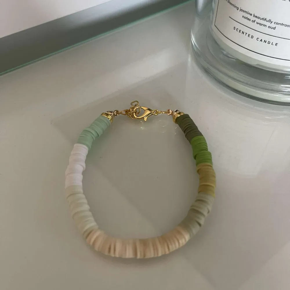 Säljer ett superfint armband med små, platta pärlor i olika gröna och beige nyanser. Armbandet har en enkel guldfärgad låsning som gör det lätt att ta på och av. Perfekt för att ge en färgklick till din outfit!. Accessoarer.