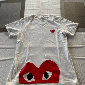 Play Comme Des Garçons T-shirt - säljer en snygg vit t-shirt från Comme des Garçons med det ikoniska röda hjärtat med ögon på bröstet och en stor röd grafik längst ner. Strl S. Skick 8,5/10. Passar till alla tillfällen!