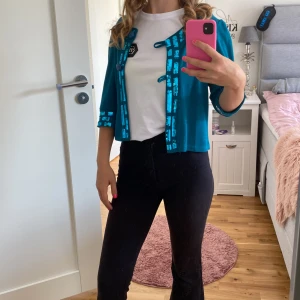 Turkos kofta med paljettdetaljer - Säljer en snygg turkos kofta med glittriga paljettdetaljer längs kanterna och ärmsluten. Koftan har trekvartsärmar och en öppen design med knytning framtill. Perfekt för att liva upp en outfit! 💙