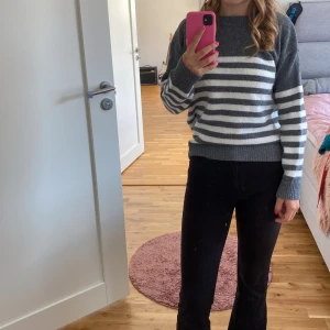 Grå och vit randig tröja - Säljer en supermysig grå och vit randig tröja. Den är perfekt för kyliga dagar med sin stickade design och långa ärmar. Tröjan har en normal passform och är gjord i ett mjukt material som känns skönt mot huden. Perfekt för både vardag och avslappnade tillfällen!