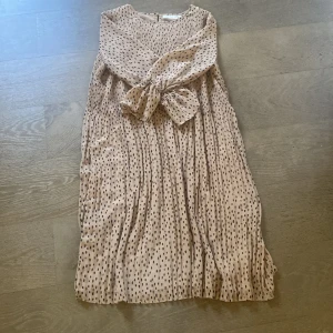 Beige prickig klänning från InWear - Säljer en superfin beige klänning från InWear med svarta prickar. Den har en söt knytning framtill och är ärmlös, vilket gör den perfekt för varmare dagar. Materialet känns lätt och luftigt, perfekt för en somrig look! 🌼