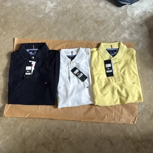Pikétröjor från Tommy Hilfiger - Säljer tre snygga pikétröjor från Tommy Hilfiger i olika färger: marinblå, vit och gul. Perfekta för både vardag och fest! De har en klassisk design med krage och knappar framtill. Märkets ikoniska logga syns diskret på bröstet.