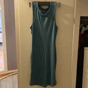 Grön ärmlös klänning - Snygg grön ärmlös klänning i en enkel och stilren design. Perfekt för att klä upp med accessoarer. Klänningen har en rak passform och är knälång.