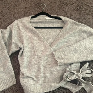 Grå omlottkofta från Even&Odd - Säljer en stilren grå omlottkofta från Even&Odd. Koftan har långa ärmar och ett knytband i midjan för en justerbar passform. Perfekt för lager-på-lager under kyligare dagar. Den är helt ny aldrig använd 