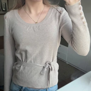 Beige tröja med knytband - Snygg beige tröja med knytband i midjan och dekorativa knappar på axlarna. Knytband i midjan som kan knytas både fram eller bak, alternativt tas bort💗
