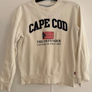 Vit tröja från The Defender - Säljer en vit tröja från The Defender med texten 'Cape Cod' och en flagga på framsidan. Perfekt för en avslappnad stil. Väldigt lite använd. 