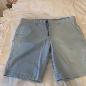 Ljusblå shorts med knapp och dragkedja - Snygga ljusblå shorts med knapp och dragkedja framtill. De har praktiska sidofickor och en bakficka med knapp. Perfekta för en avslappnad stil.