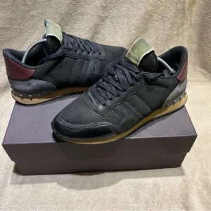 Valentino rockrunners - Tja säljer ett par svarta Valentino rockrunners med pytte små defekter som nu är lagade. Skorna har en unik design med en mörkröd häl och grå detaljer. Längst fram på skon är det limmat väldigt fint eftersom dom blev inskickade på lagning. Och det syns självklart inte. Du hittar de på sista bilden👍🏼