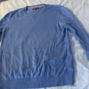 Blå tröja från Tommy Hilfiger - Säljer en stilren blå tröja från Tommy Hilfiger. Tröjan har en rund halsringning och långa ärmar. Perfekt för en  simpel still eller ha hemma. Liten fläk på långärmad men syns knappt!