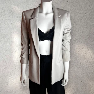 H&M Beige kavaj - Snygg beige kavaj från H&M  med normal passform och långa ärmar. Perfekt för en stilren look. Kavajen har en klassisk design med krage och är tillverkad i ett mjukt material.