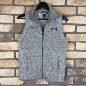Patagonia väst - Säljer en snygg grå fleeceväst från Patagonia med dragkedja och broderad logga. Perfekt för lager-på-lager under kyliga dagar. Västen har en stilren design med två praktiska fickor framtill.