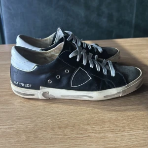 Svarta sneakers från Philippe Model - Snygga svarta sneakers från Philippe Model med vita detaljer och snörning. Skorna har en klassisk design med en vit sula och märkeslogga på sidan. Perfekta för en stilren look.