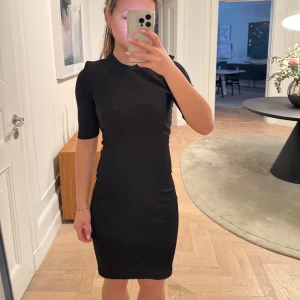 Svart klänning med korta ärmar - Snygg svart klänning i tight passform med korta ärmar. Perfekt för en stilren look. Klänningen är enkel och elegant, vilket gör den lätt att matcha med olika accessoarer.