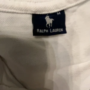 Vit pikétröja från Ralph Lauren - Säljer en klassisk vit pikétröja från Ralph Lauren med den ikoniska loggan broderad på bröstet. Tröjan har en krage och knappar framtill, perfekt för en stilren look. Passar både till vardags och mer uppklädda tillfällen.