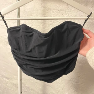 Korsett topp - Snygg svart korsett topp  med dragkedja bak. Toppen har en stilren design med rynkade detaljer framtill som ger en elegant look. Perfekt för en kväll ute eller en speciell tillställning.