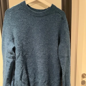 Blå stickad tröja - Säljer en mysig blå stickad tröja med rund hals och långa ärmar. Perfekt för kyliga dagar och ger en stilren look. Hör av dig vid intresse! Från arket