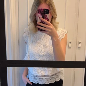 Vit spetsblus från Only - Säljer en söt vit spetsblus från Only med vackra detaljer. Blusen är ärmlös och har en fin spetsdesign med volangdetaljer vid ärmarna och nederkanten. Enbart använd 3/4 gånger 