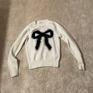 Vit tröja med svart rosett - Fin stickad tröja från Holly & Whyte. Strl. XS.   OBS kan ej skicka med Instabox endast PostNord