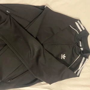 Svart träningsjacka från Adidas - Säljer en svart träningsjacka från Adidas med dragkedja och de klassiska tre ränderna på jackan. Storlek S och den är i jättegod skick. 