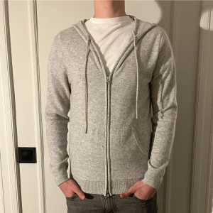 Grå kashmir hoodie från John Henric - Säljer en stilren grå hoodie i mjuk kashmir från John Henric. Tröjan har dragkedja framtill och praktiska fickor. Ny pris 2500-mitt pris 1600kr-modellen är 185cm och väger 70kg