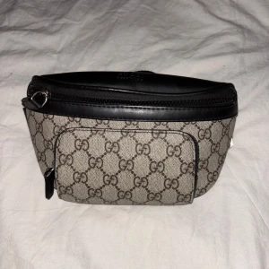 Mönstrad magväska från Gucci - Säljer en stilren magväska från Gucci med det klassiska GG-mönstret. Väskan har en justerbar rem och flera dragkedjeförsedda fack för säker förvaring. Dom 3 olika facken för det enkelt att hålla dina saker organiserade och lättillgängliga. Skriv vid fler frågor och priset är självklart inte hugget i sten!