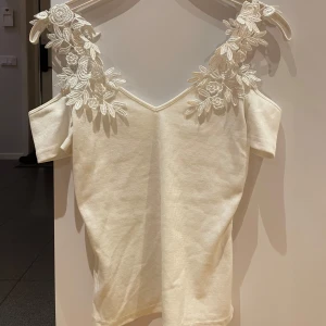 Vit ribbad topp med spetsdetaljer - Säljer en söt vit ribbad topp med vackra spetsdetaljer på axlarna. Toppen har en offshoulder-design och korta ärmar, perfekt för sommarens varma dagar. Den är både stilren och romantisk, vilket gör den till ett måste i garderoben.