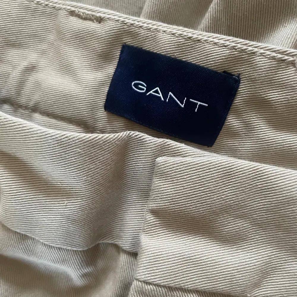 Snygga beige chinos från GANT i klassisk stil. De har en rak passform och är tillverkade i ett bekvämt bomullsmaterial. Perfekta för en stilren look.. Farkut & Housut.