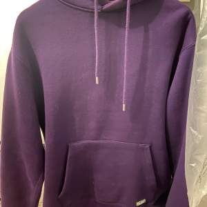 Säljer en snygg lila hoodie med känguruficka framtill. Den har en justerbar huva med dragsko och långa ärmar. Perfekt för en avslappnad stil.