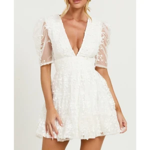 Vit klänning från Showpo - Säljer en superfin vit klänning med v-ringning och broderade blommor. Den har korta puffärmar och en dragkedja i ryggen. Perfekt för studenten💕 Säljer pga att den var för liten, helt oanvänd med prislapp kvar. Slutsåld på hemsidan. Köptes för 1450kr inklusive frakt och taxes☺️