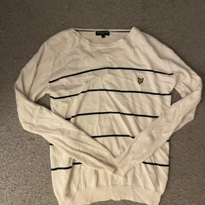 Vit tröja från Lyle & Scott - Säljer en stilren vit tröja från Lyle & Scott med svarta ränder och deras ikoniska gula logga på bröstet. Tröjan har långa ärmar och en klassisk passform. Hör gärna av er vid funderingar:)