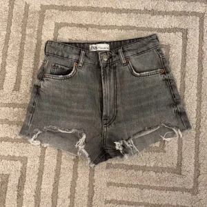 Grå jeansshorts från Zara - Snygga grå jeansshorts från Zara med slitna kanter och klassisk femficksdesign. Perfekta för en avslappnad stil. Tillverkade i 100% bomull för en bekväm passform. Mycket bra skick storlek 34