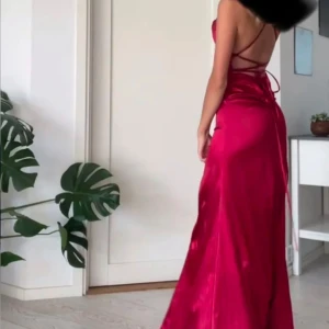 Röd långklänning med slits - Snygg röd långklänning stl S med en elegant slits framtill. Klänningen har smala axelband och en öppen rygg med snörning som ger en fin detalj. Perfekt för en festlig kväll! Knappt använd.    (Inte mina bilder) 