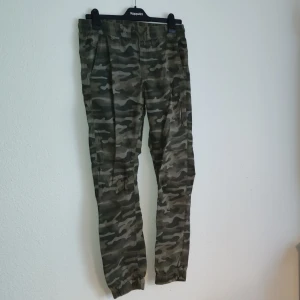 Camouflage cargobyxor från KappAhl - Snygga camouflage cargobyxor från KappAhl med elastisk midja och praktiska fickor. Perfekta för en avslappnad stil med en militär touch. Byxorna har en klassisk camo-look som aldrig går ur tiden.