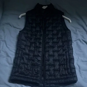 Svart dunväst från Everest - Säljer en svart dunväst från Everest. Västen har en dragkedja framtill och är perfekt för kyligare dagar. Den är lätt och isolerande, vilket gör den idealisk för höst och vår. Passar bra för en casual look.