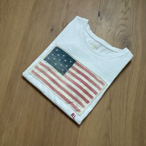 Vit t-shirt från Ralph Lauren - Tja! Säljer en riktigt fet tisha från Ralph Lauren. Slitningarna på flaggan är en del av designen, riktigt snyggt enligt mig. Storlek S. Hör av dig vid frågor eller liknande✌️