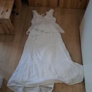 Vitt kjol med en blus  storlek 140 - Säljer en vacker vit långklänning med volangdetaljer och knytning i ryggen. Klänningen har en luftig och flödande design, perfekt för varma dagar. Den är ärmlös och har en romantisk känsla. Perfekt för sommarens alla tillfällen! 🌸