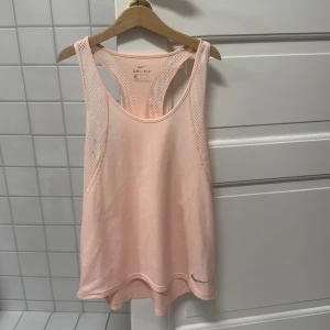 Ljusrosa linnetopp från Nike - Säljer en ljusrosa linnetopp från Nike med Dri-FIT-teknologi. Toppen har en sportig design med meshdetaljer på sidorna för extra ventilation. Perfekt för träning och varma dagar.