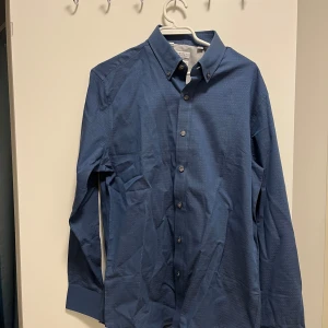 Blå skjorta från Brunello Cucinelli - Snygg blå skjorta från Brunello Cucinelli med leisure fit. Skjortan har långa ärmar och knappar framtill. Perfekt för en stilren look. Oanvänd skick 10/10.