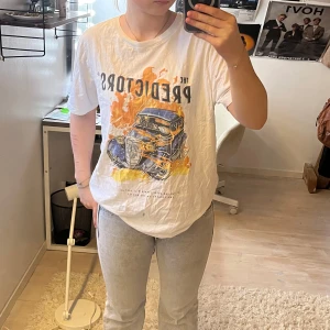 Vit t-shirt med tryck från Smog - Säljer en vit t-shirt från Smog med ett coolt tryck av en bil och texten 'The Predictors' i orange och blått. T-shirten har en normal passform och korta ärmar. Perfekt för en avslappnad stil. Står storlek L, men tycker själv att den snarare sitter som M.
