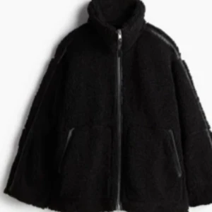 Svart teddyjacka med dragkedja - Mysig svart teddyjacka med hög krage och dragkedja framtill. Perfekt för kyliga dagar med sin mjuka och varma känsla. Jackan har långa ärmar och två praktiska fickor framtill.