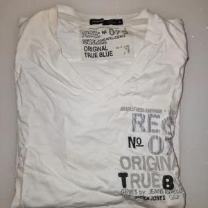 Vit t-shirt från Jack & Jones - Säljer en vit t-shirt från Jack & Jones med tryck i grått och svart. T-shirten har en v-ringad hals och korta ärmar. Perfekt för en avslappnad stil. Garderobsrensning så kika gärna på övriga auktioner.