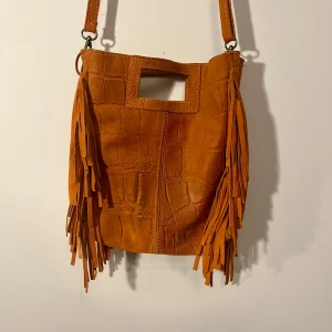 Maje-inspirerad väska  - Så cool orange maje-inspirerad väska i läder/fejkläder med fransar och krokodilmöster, perfekt för att spicea upp en outfit🤩Köpt på en marknad i Spanien. Lite missfärgningar som syns på bild 3