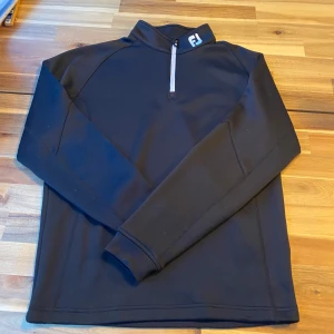 Halfzip FootJoy - Säljer en svart tröja från FootJoy i storlek S. Tröjan har en dragkedja vid halsen och är tillverkad i 100% polyester. Perfekt för en sportig look med långärmade ärmar och en stilren design. Nypris ca 1000kr använd fåtal gånger inga defekter